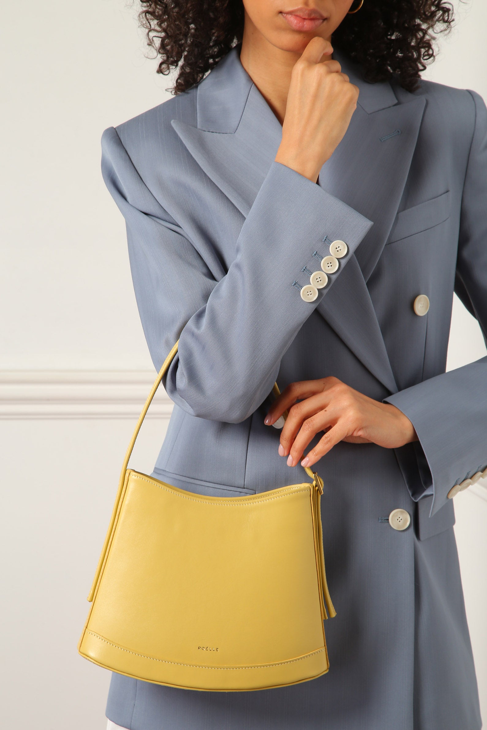 Luxury minimalist leather bag in yellow held by woman wearing a tailored blue blazer from Poelle Atelier