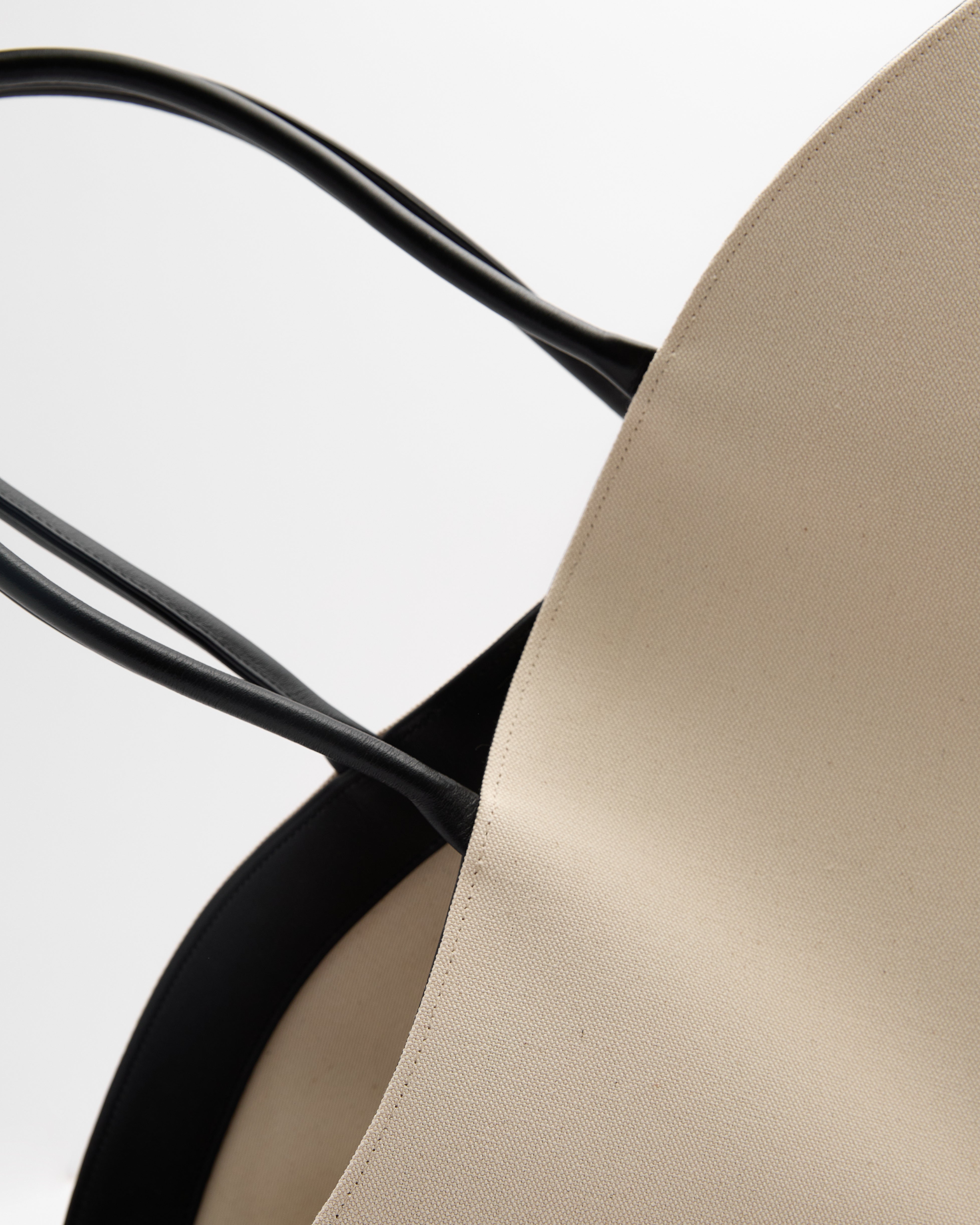 Close-up of Poelle Atelier luxury summer leather bag showing smooth beige leather and black handles