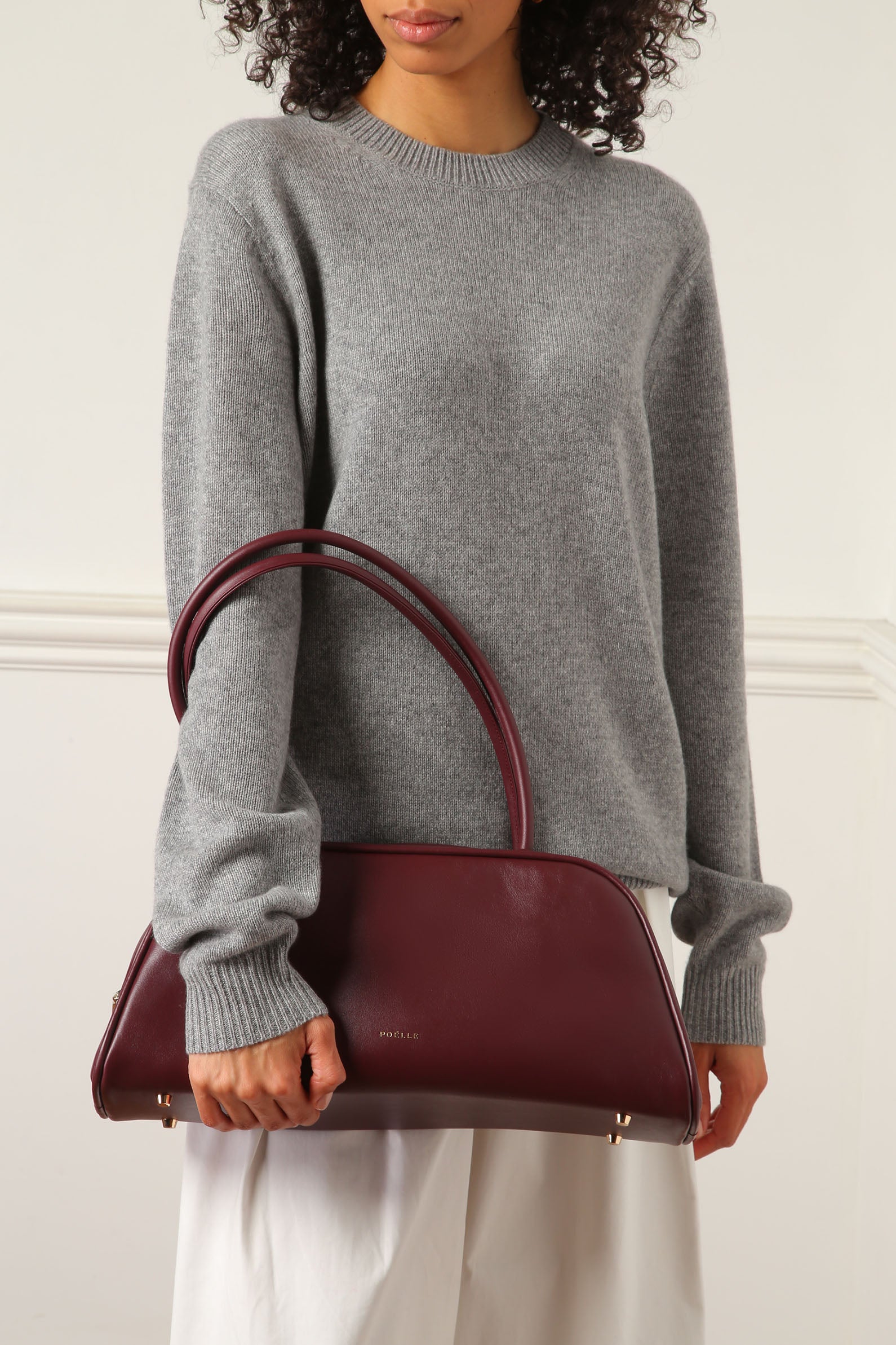 Poelle Atelier burgundy leather east-west horizontal bags carried by woman in gray sweater