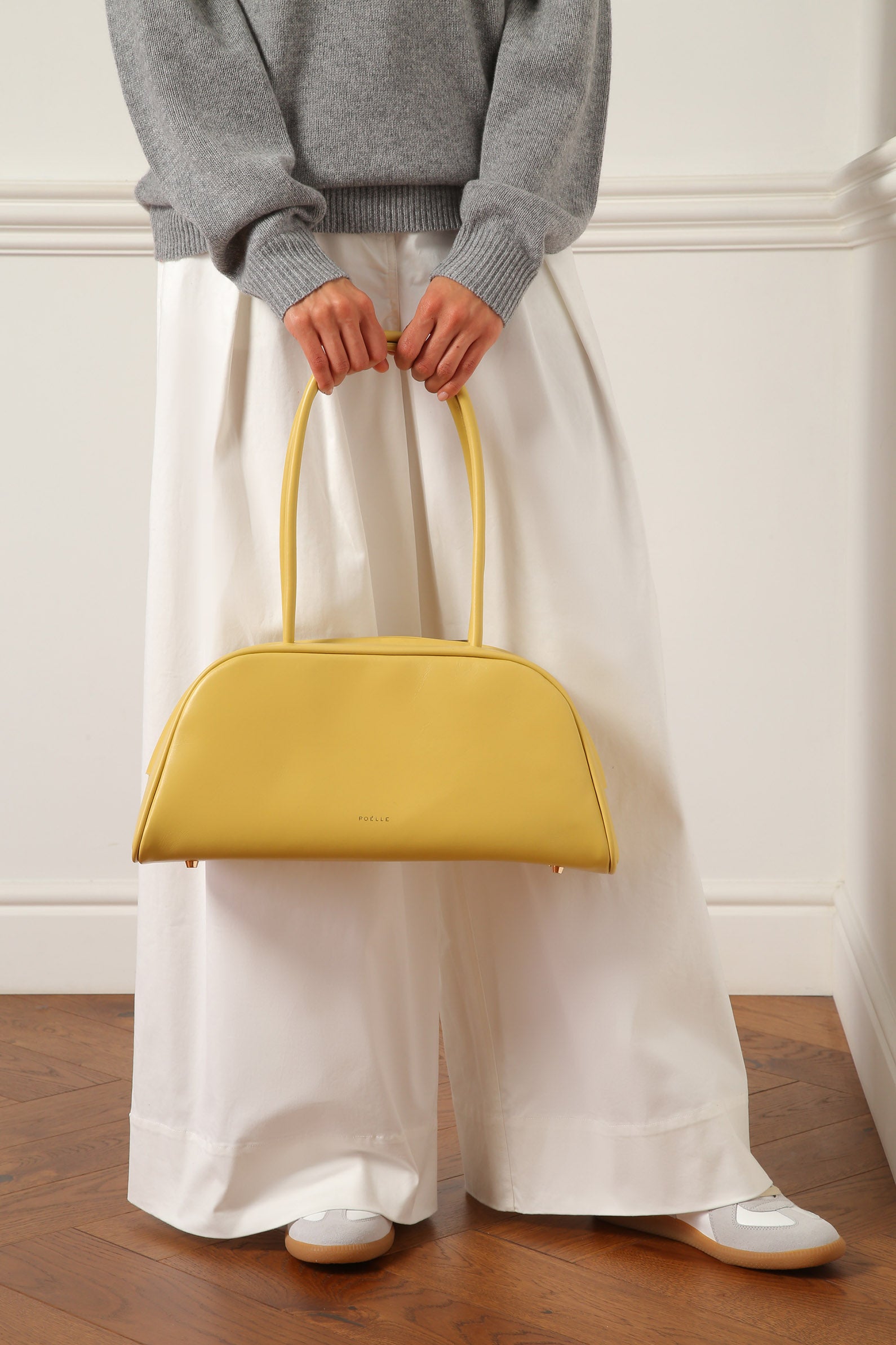 Yellow east-west horizontal bags by Poelle Atelier held by person in gray sweater and white pants