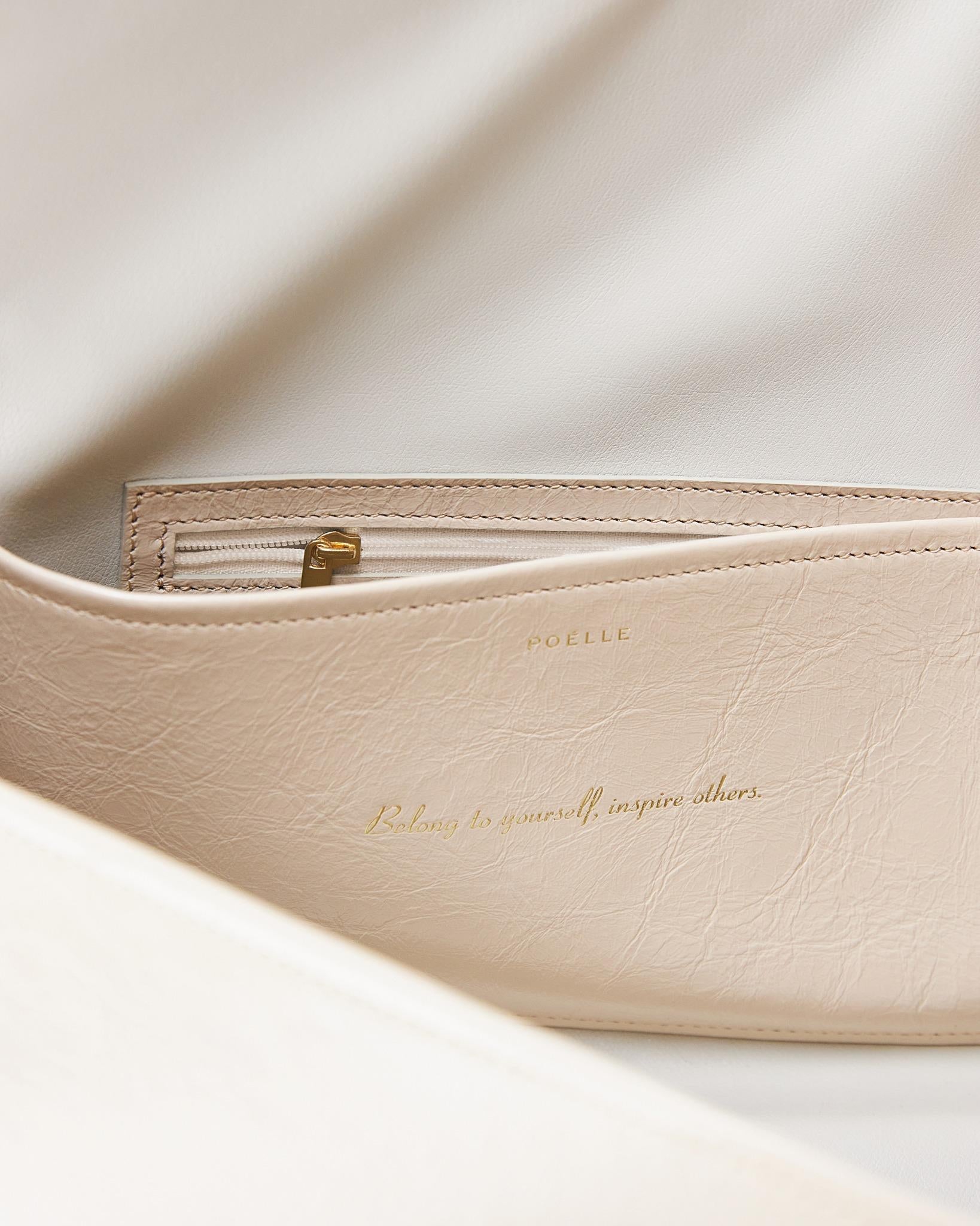 Close-up detail of Poelle Atelier high-end fashion leather bag in cream with gold zipper and embossed logo