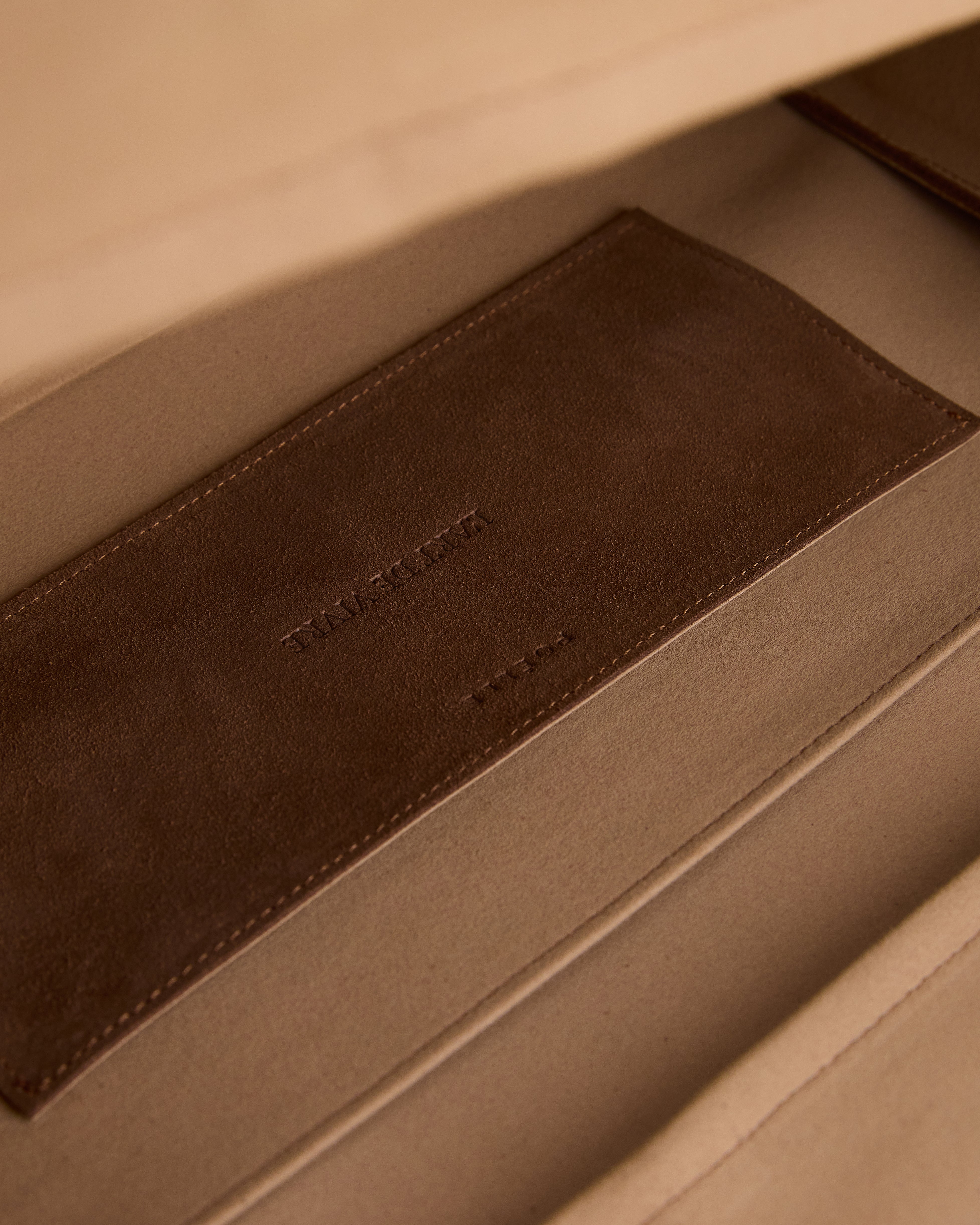Close-up of brown leather label inside luxury suede tote bag by Poelle Atelier showing fine stitching and material texture