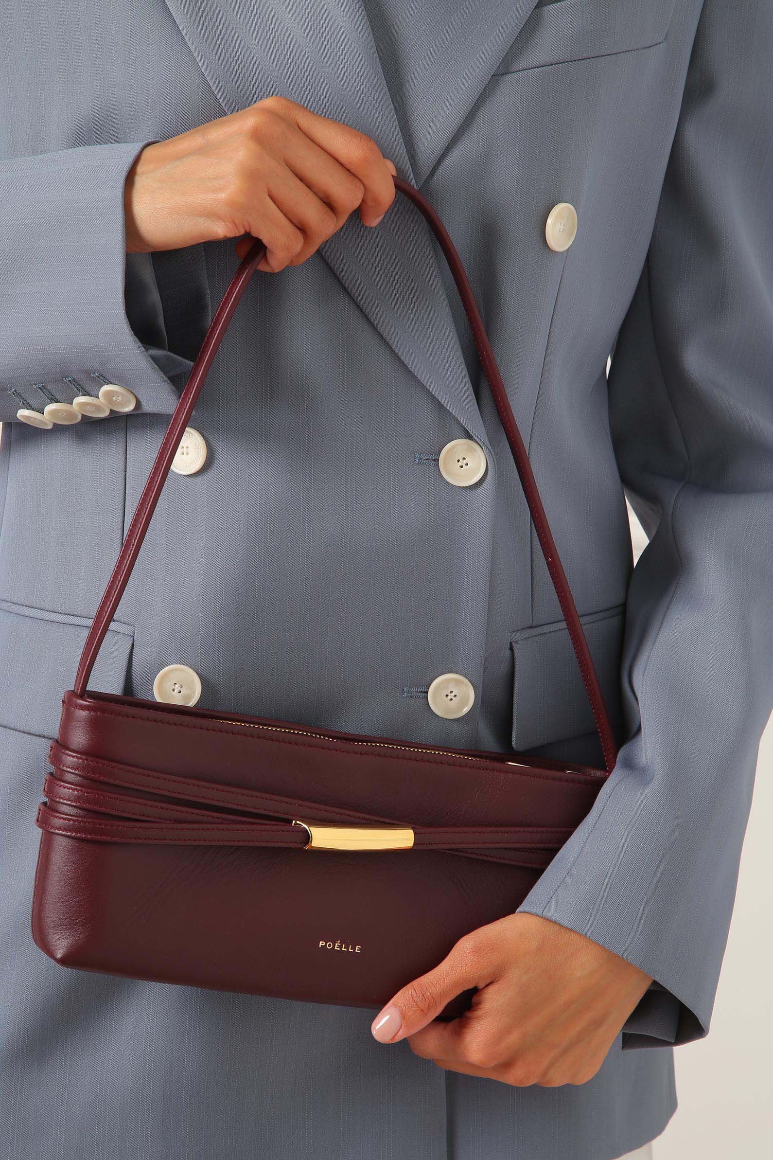 Marsala leather shoulder bag by Poelle Atelier held by woman wearing gray blazer