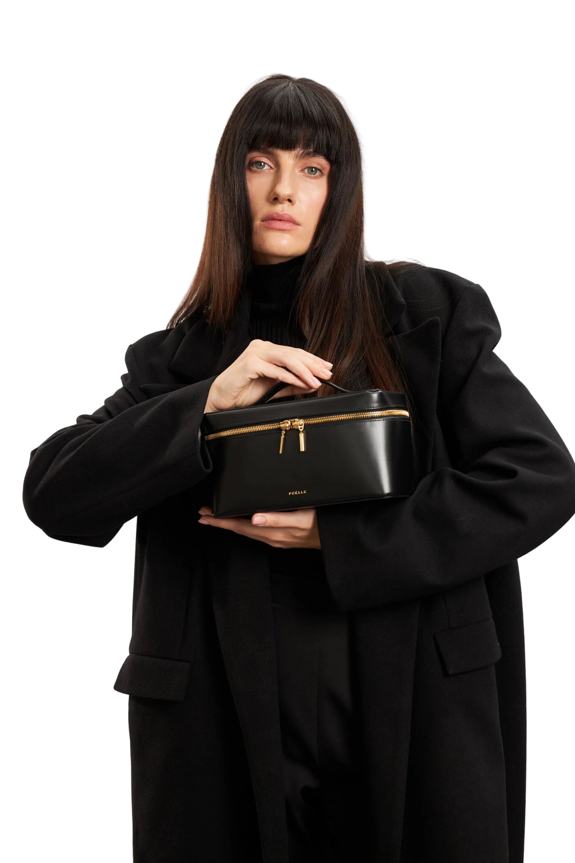 Poelle Atelier medium leather makeup case in black with gold zipper held by woman in black coat