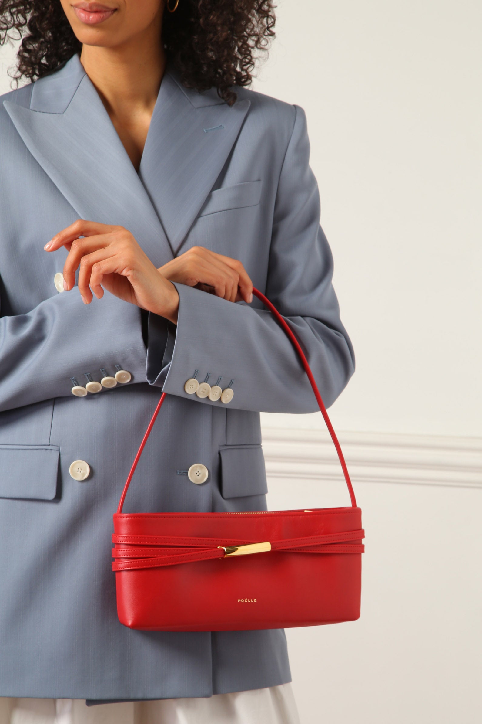 Poelle Atelier red leather shoulder bag with gold accent held by woman in blue blazer