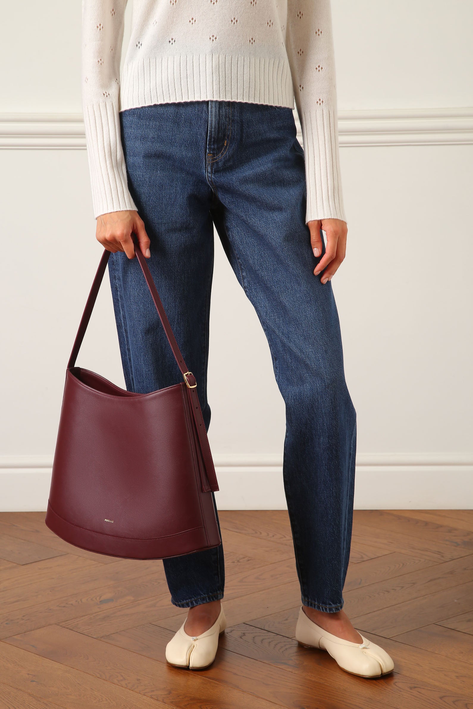 Poelle Atelier luxury minimalist sculptural bag in burgundy leather held by woman wearing jeans and white sweater