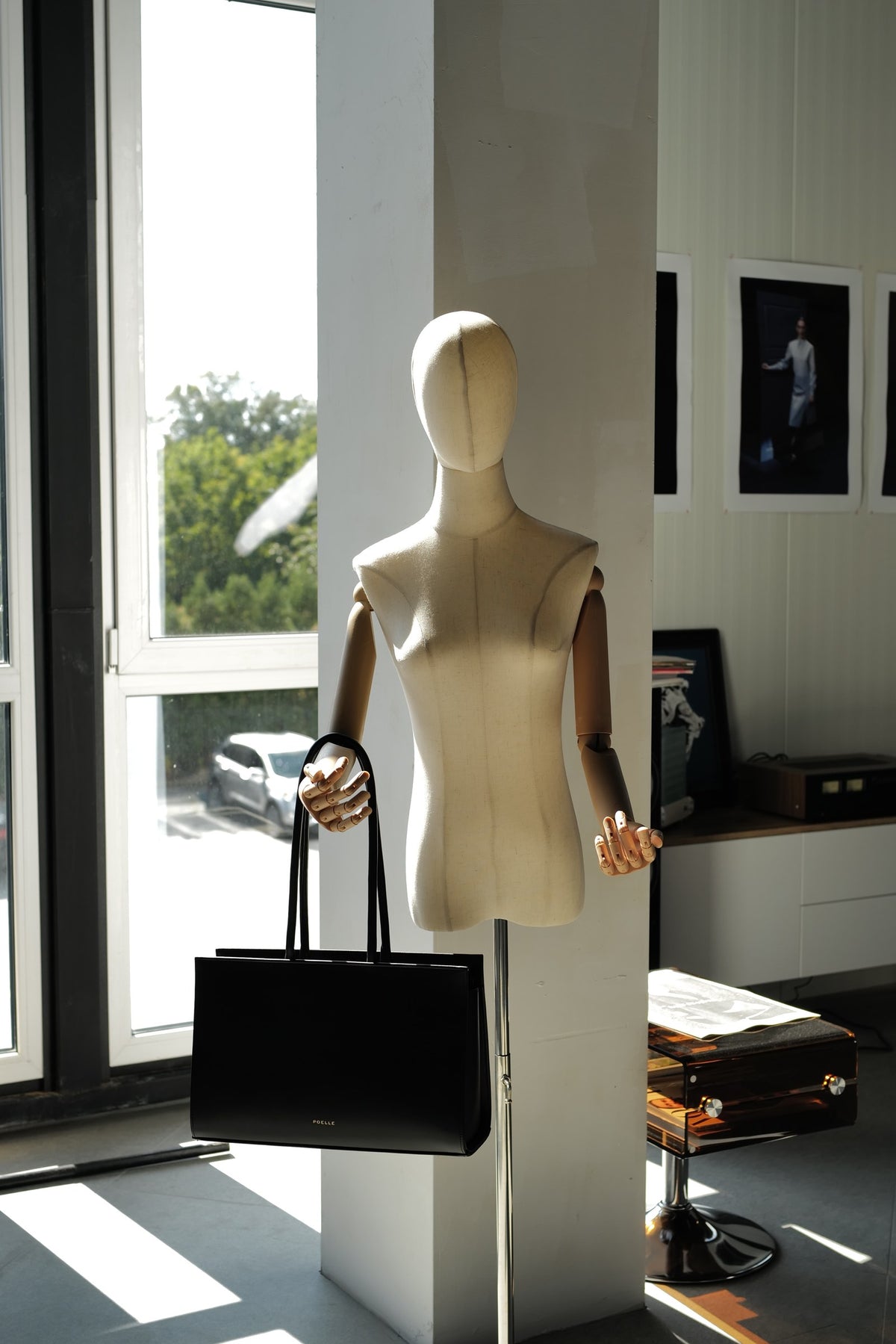 A mannequin holding a black Carolyn bag by the atelier window