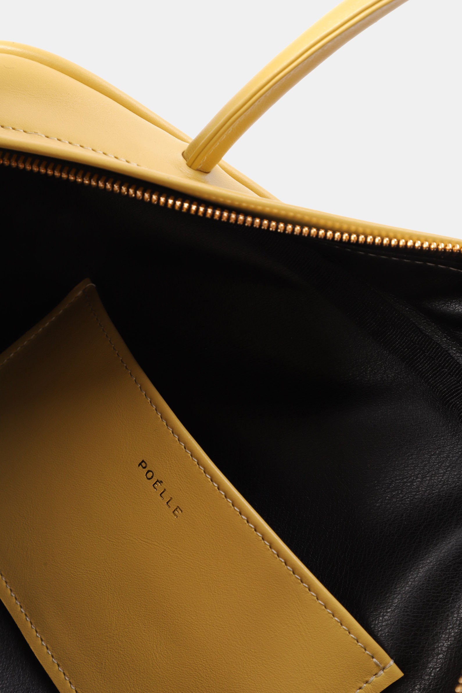 Close-up of Poelle Atelier east-west horizontal bags showing yellow leather interior pocket and gold zipper